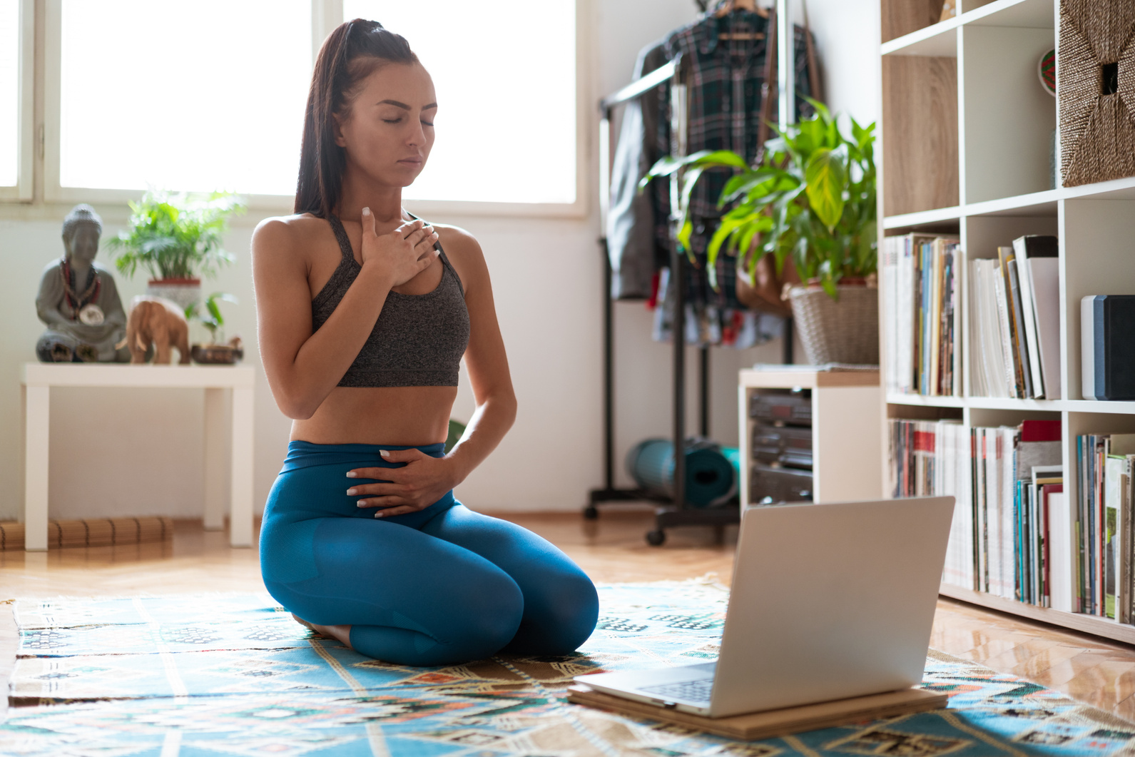 Young woman following online yoga class and doing her breathing exercises at home